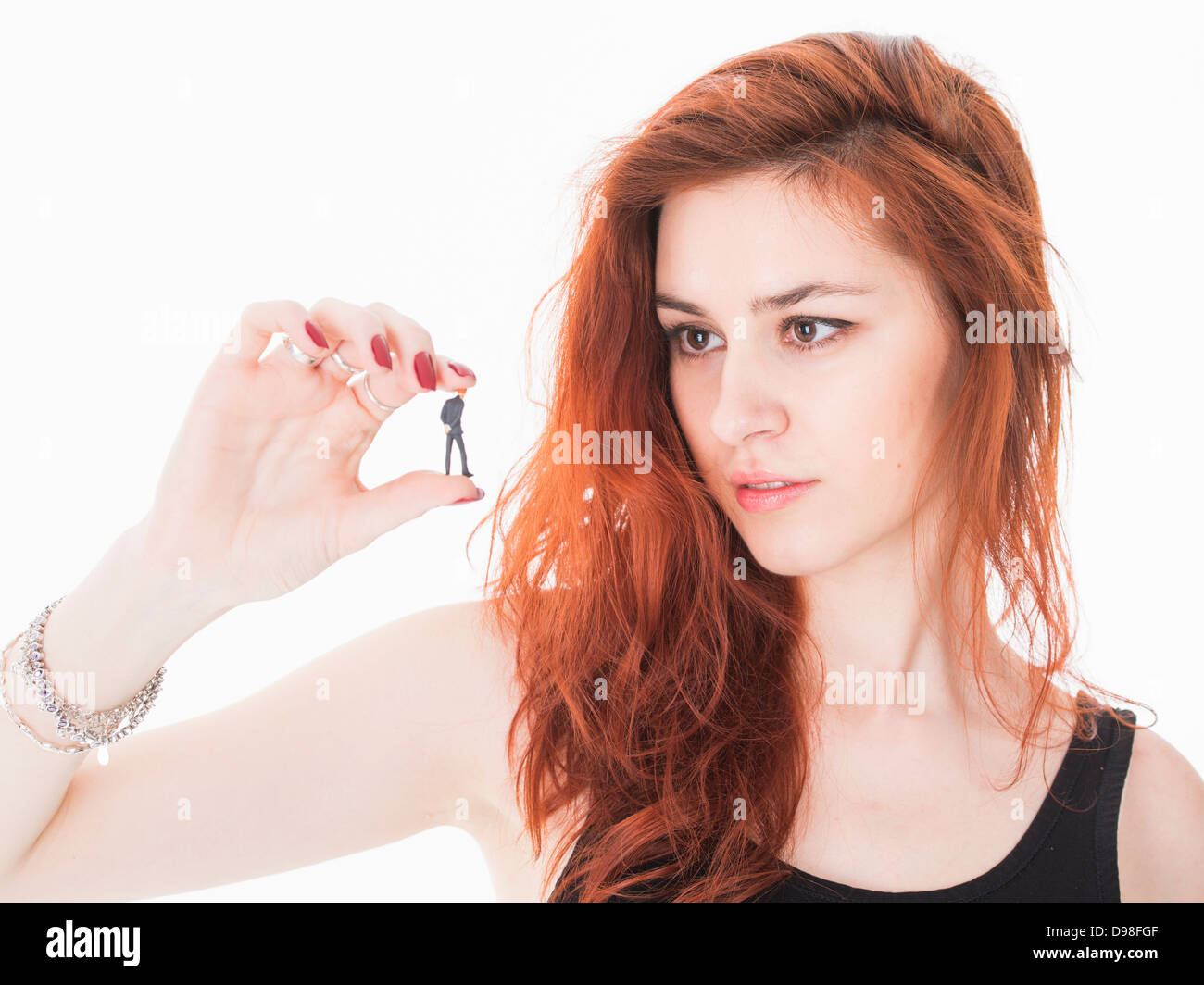 Young red haired woman in her 20s holding miniature figurine of businessman. Stock Photo