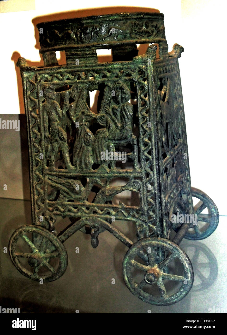 Bronzed wheeled stand with an animal frieze on the ring and figures in the side panels.  Made in Cyprus, 13th or 12th century BC.  The panels principally show ; a seated harp-player approached by a musician and a serving boy; a winged sphinx, a lion gripping a water by its neck, and a chariot. Stock Photo