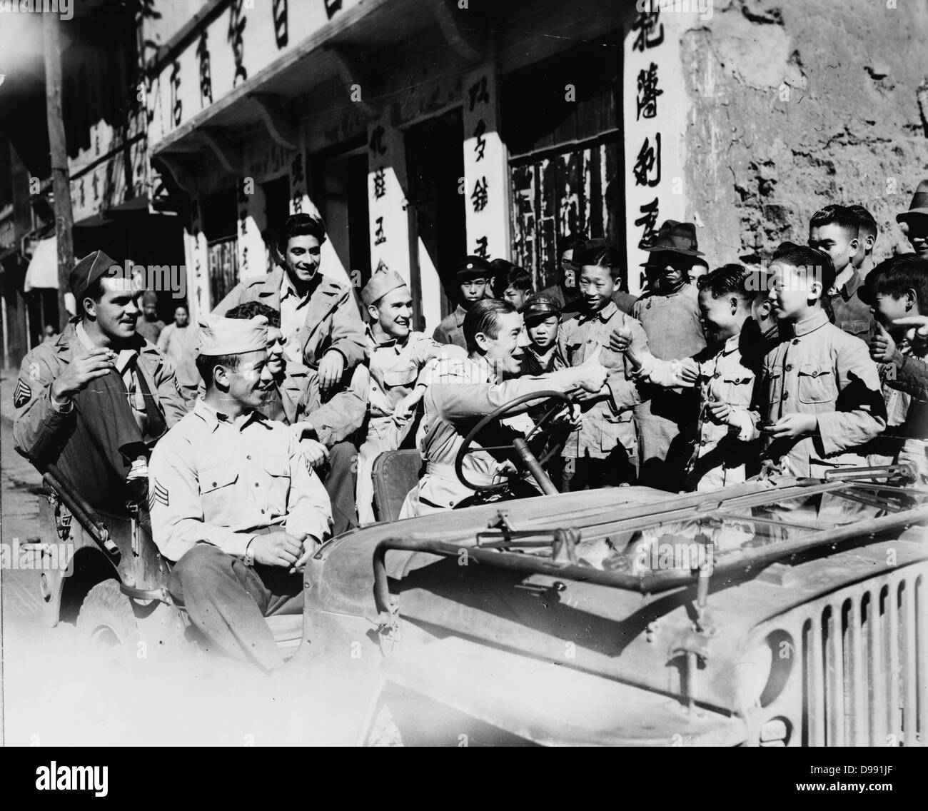 Joe E Brown (1892-1973) American actor and comedian driving jeep loaded with American GIs seeing the sights in China. Brown giving thumbs up sign to Chinese children, 1942 or 1943. Stock Photo