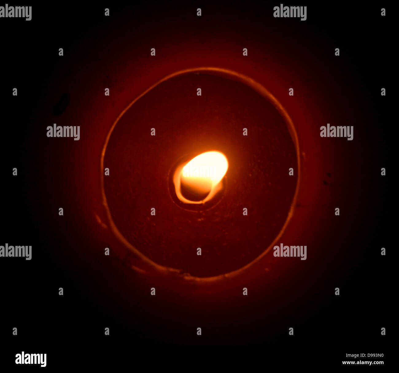 A red candle burns. Shown from above the flame is melting the wax to