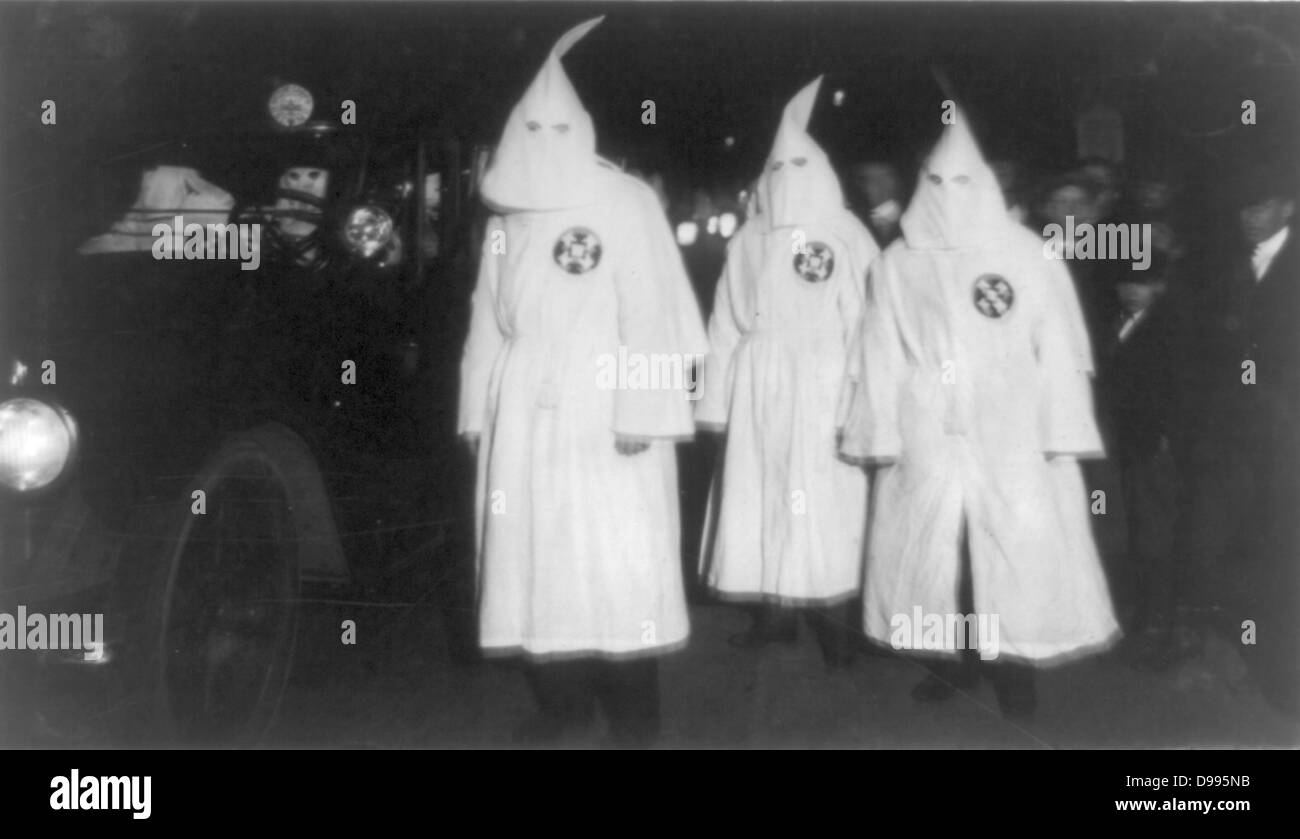 Three Ku Klux Klan members standing beside automobile driven by Klan members.  1922 March Stock Photo