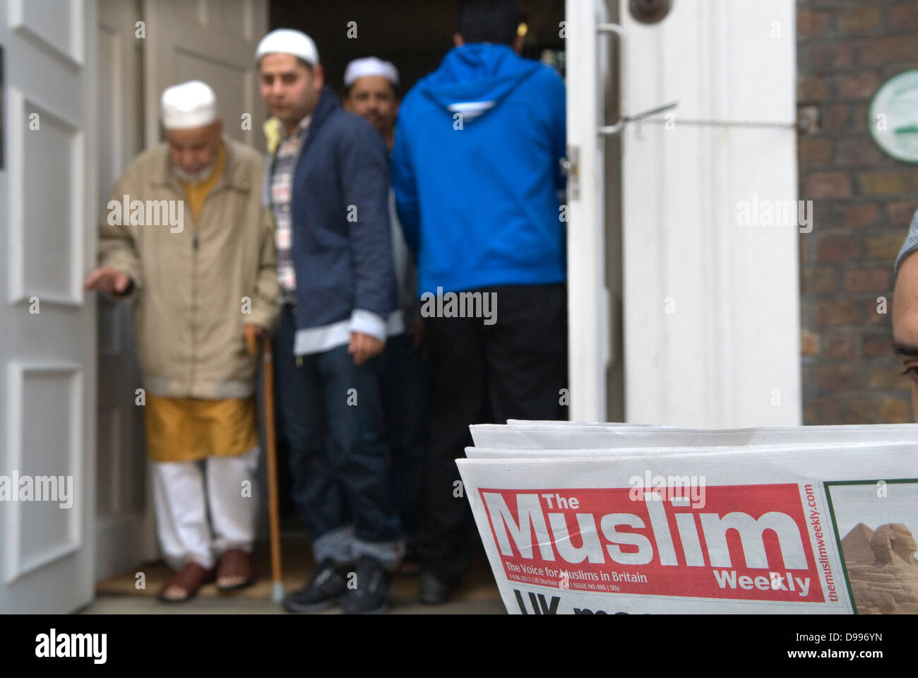 Men leaving Friday Prayers Jamme Masjid Mosque, Brick Lane, London E1. Man reading a free copy of The Muslim, The Voice of Muslims 2013 UK 2010s HOMER SYKES Stock Photo