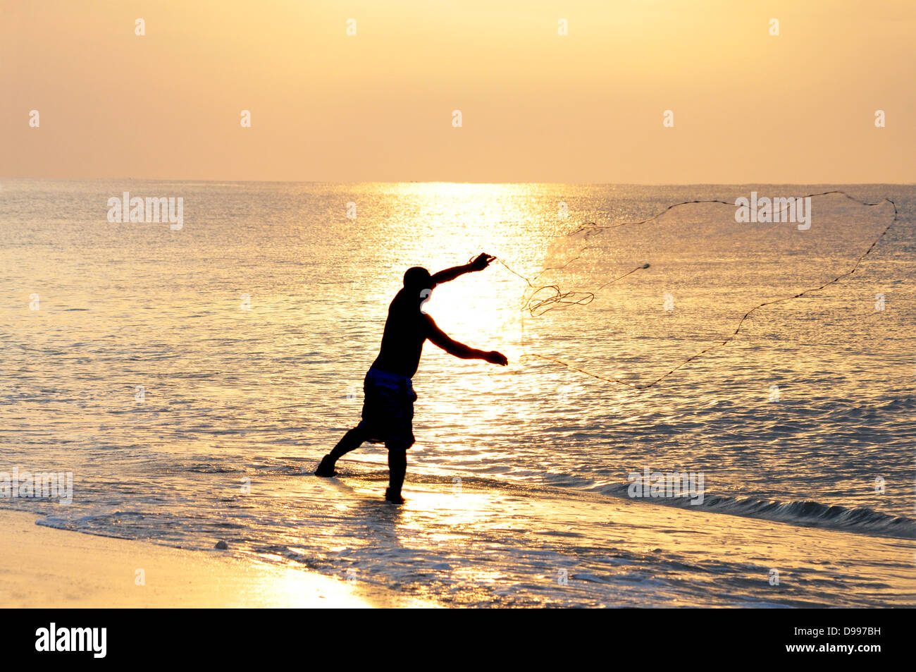 Young fisherman throwing a fishing net into the ocean Stock Photo