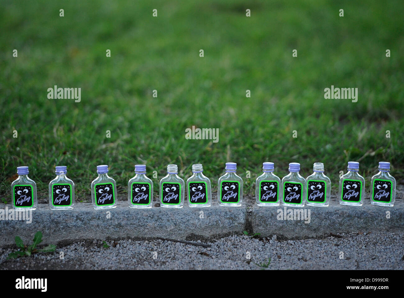 Row of empty schnapps bottles small coward vodka lined up on kerbstone Stock Photo