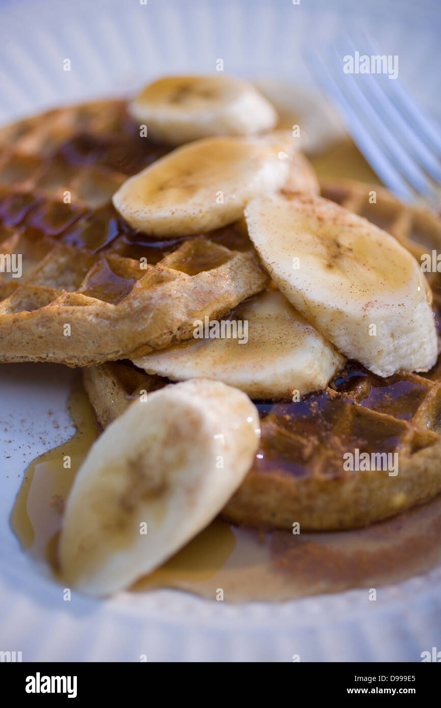 two whole wheat waffles maple syrup sliced bananas on a round plate Stock Photo