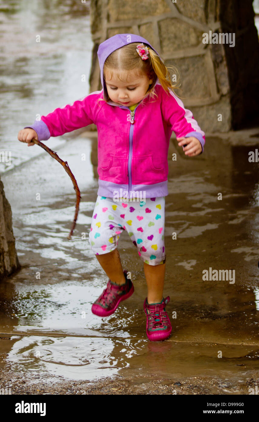 A two year old girl jumps into a mud puddle. Stock Photo