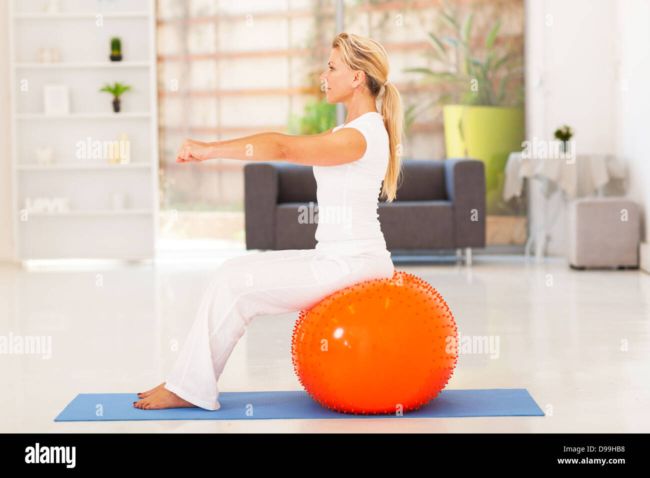 fit middle aged woman sitting on exercise ball at home Stock Photo
