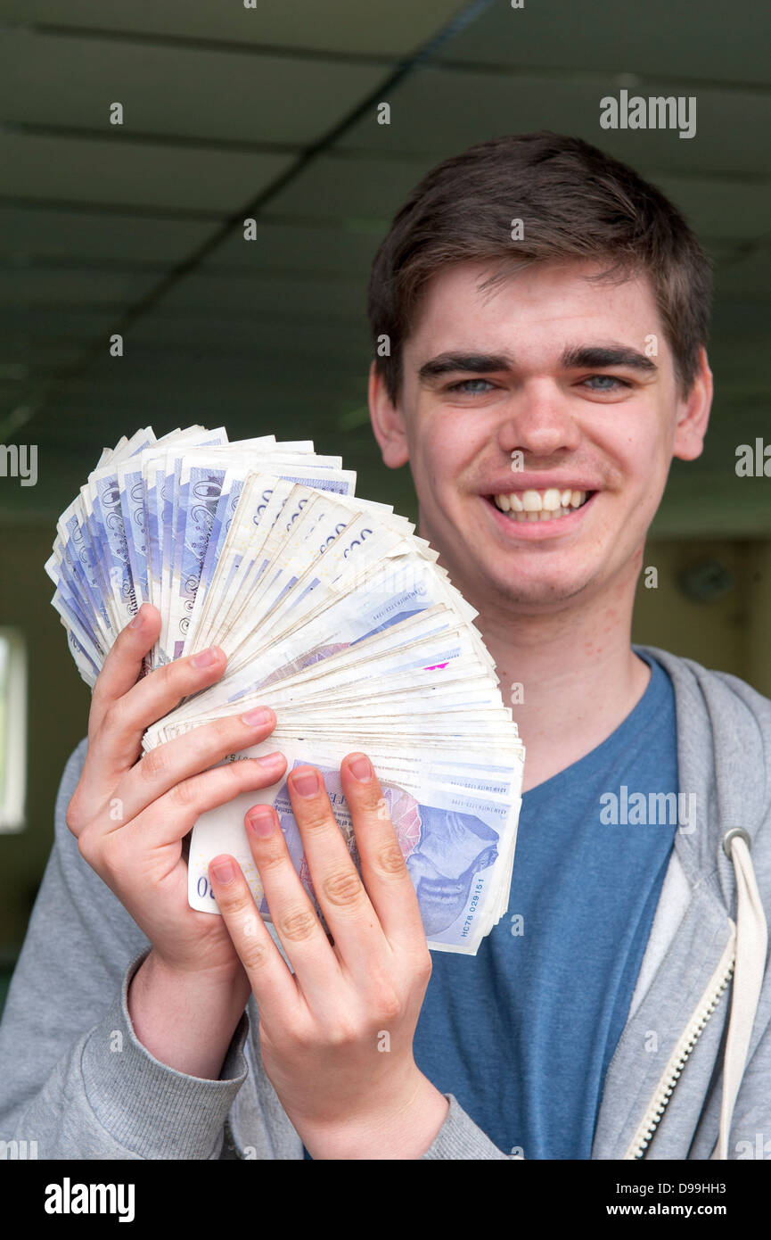 happy young man holding a fan of twenty pound notes totaling three thousand pounds Stock Photo