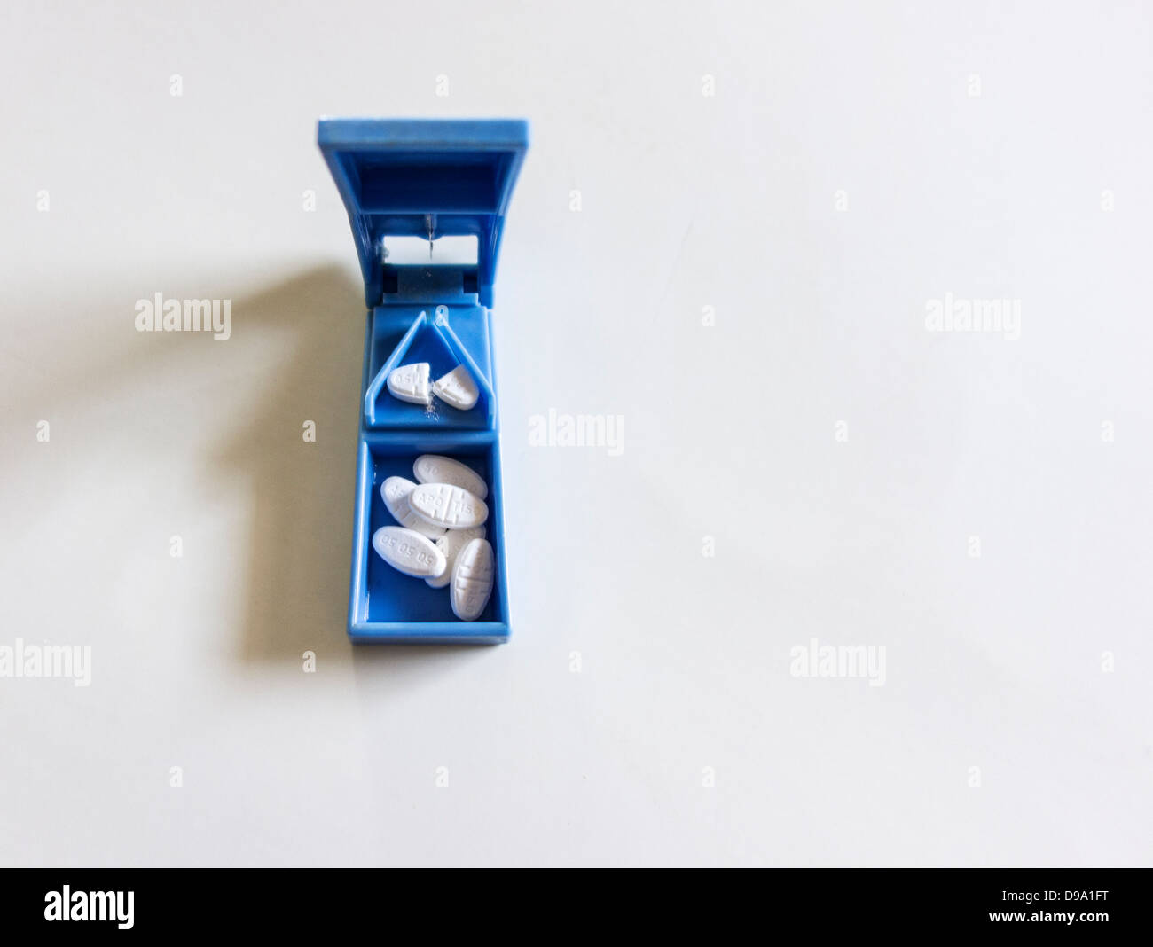 A blue plastic pill splitter with pills inside on a white background ...