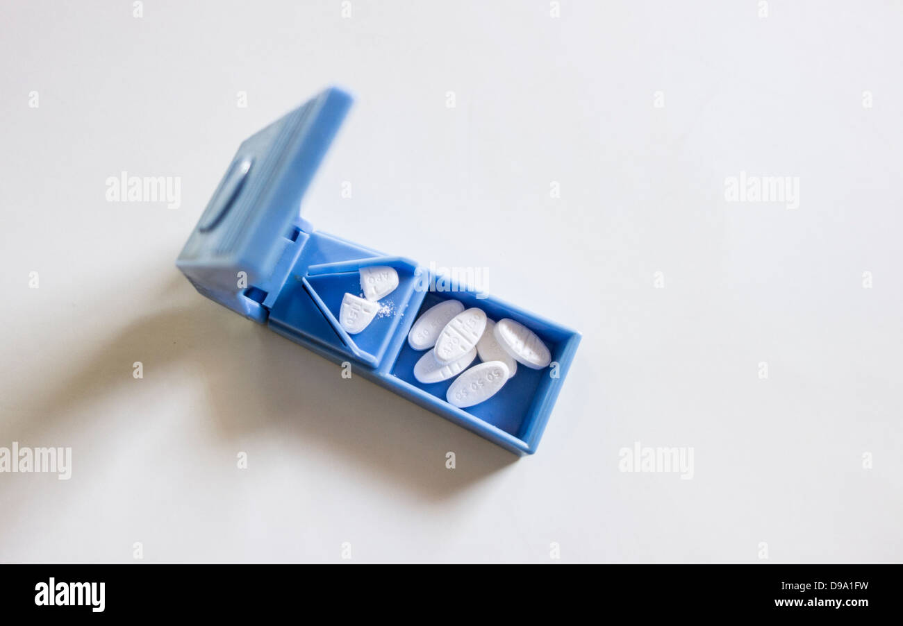A blue plastic pill splitter with pills inside on a white background ...