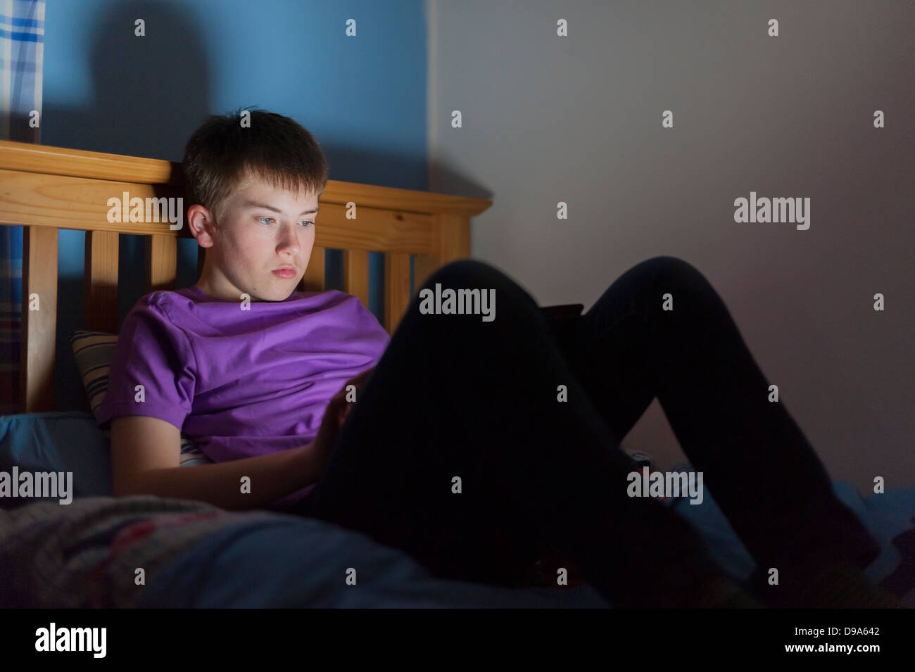 A 13 year old teenage boy using a tablet on the in bed Stock