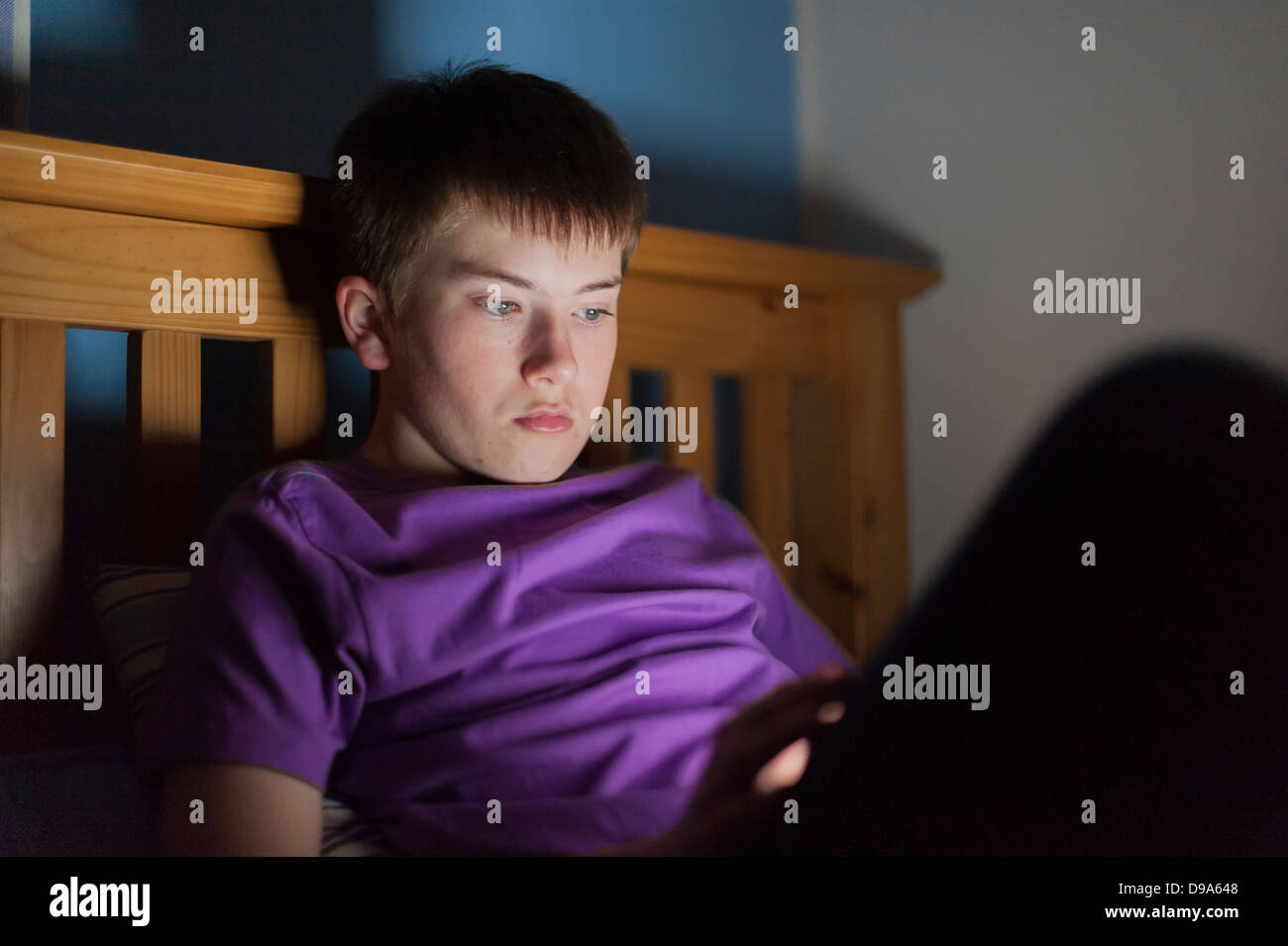 A 13 year old teenage boy using a tablet on the in bed Stock