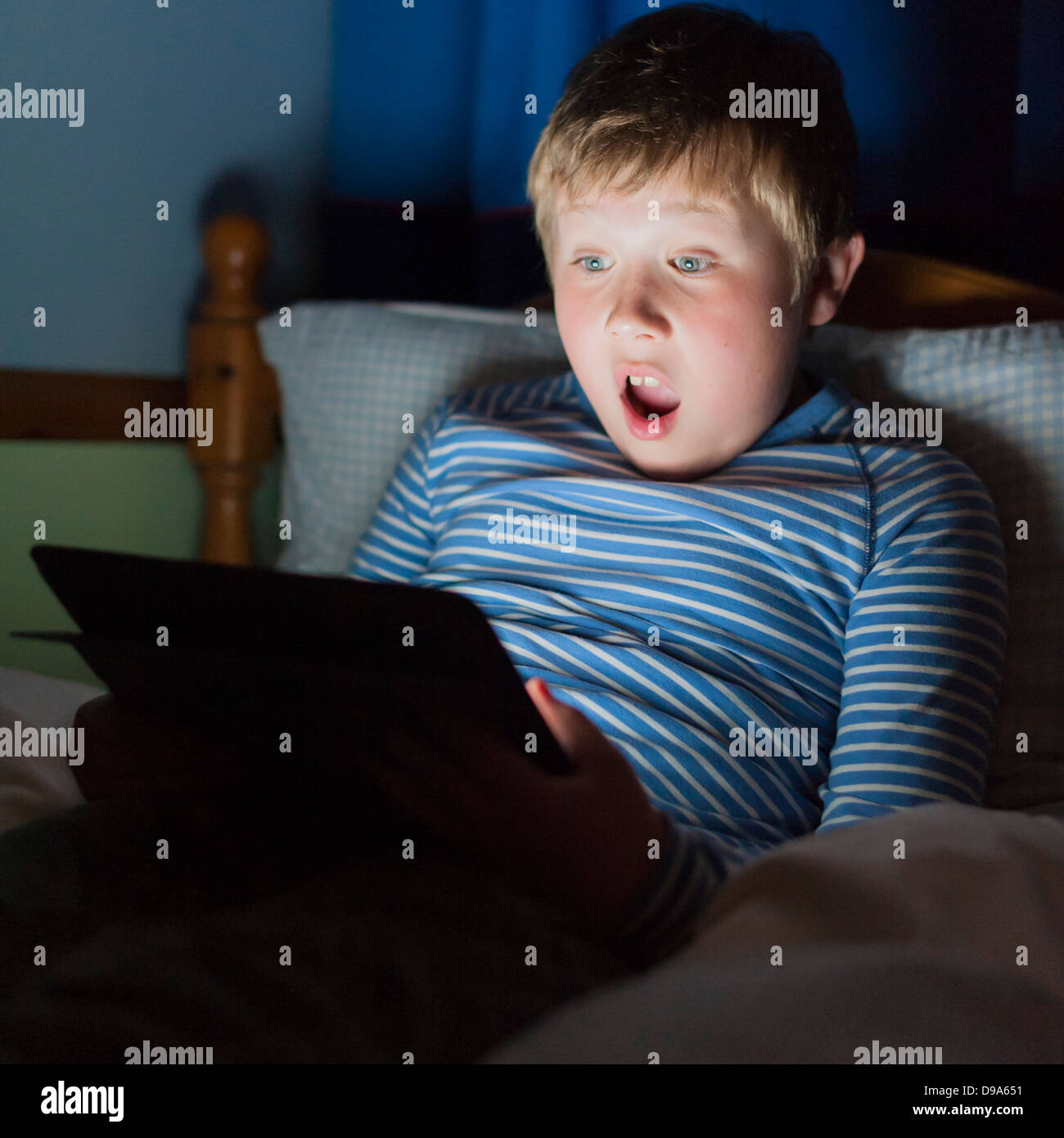 A 9 year old boy using a tablet on the internet in bed Stock Photo