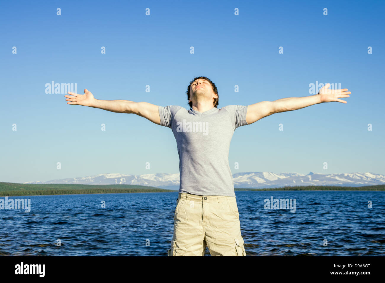 Man traveller standing outdoor with his hands raised to the blue sky northern landscape mountain and sea on background Freedom Stock Photo