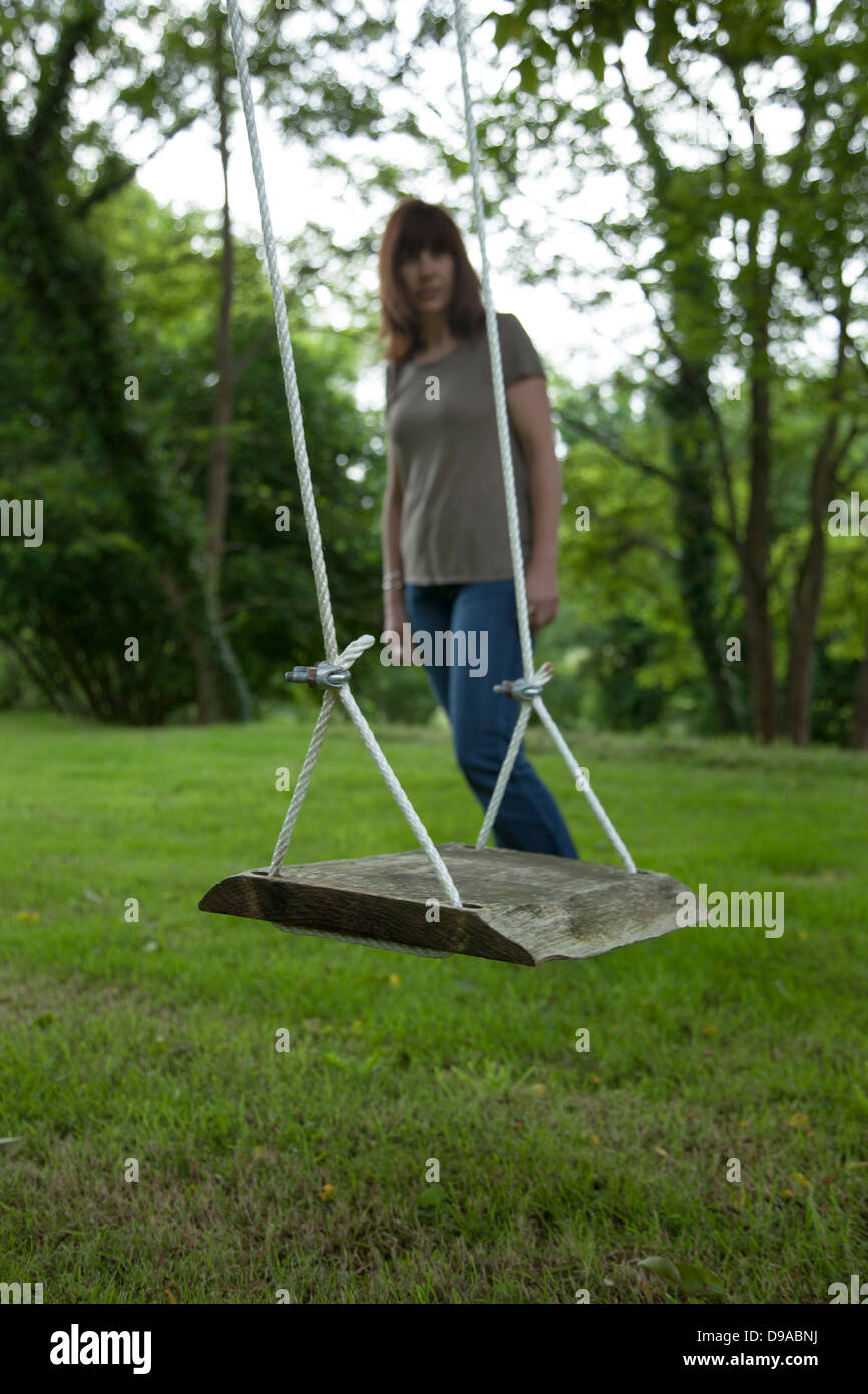 A pensive woman looking at an empty garden swing. Stock Photo