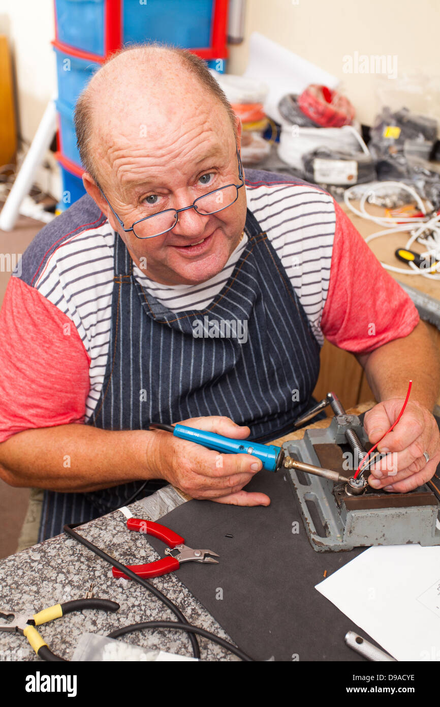 happy senior technician working with soldering iron in workshop Stock Photo