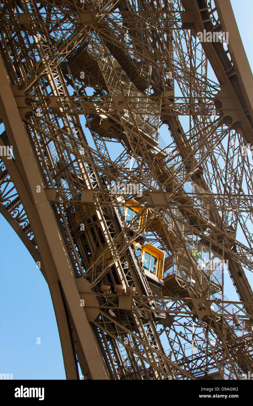 Two bright orange elevators climbing Eiffel Tower girder as tourists walk down adjacent steps Stock Photo