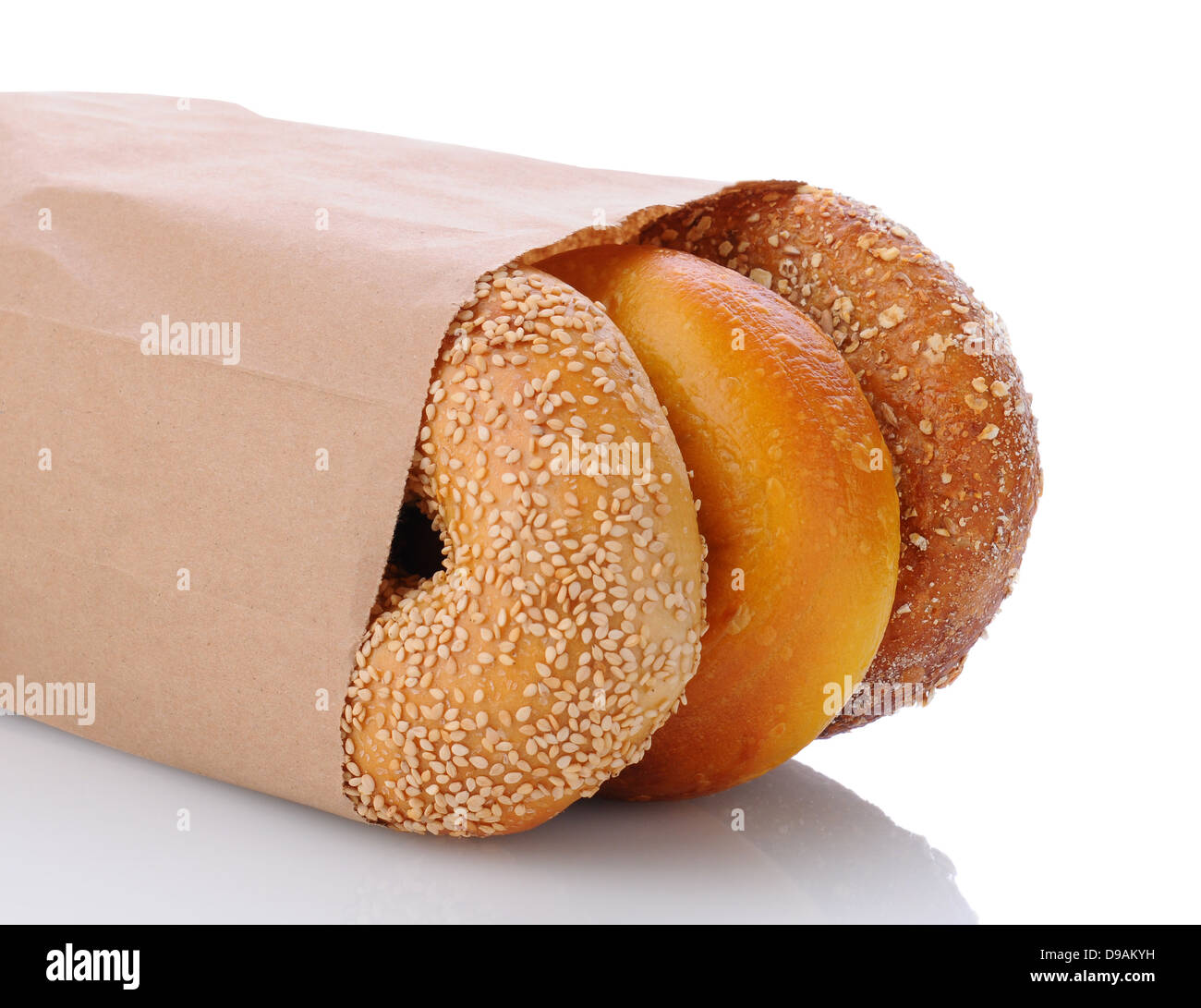 Closeup of three bagels in a brown paper bag laying on its side. Horizontal format on white with