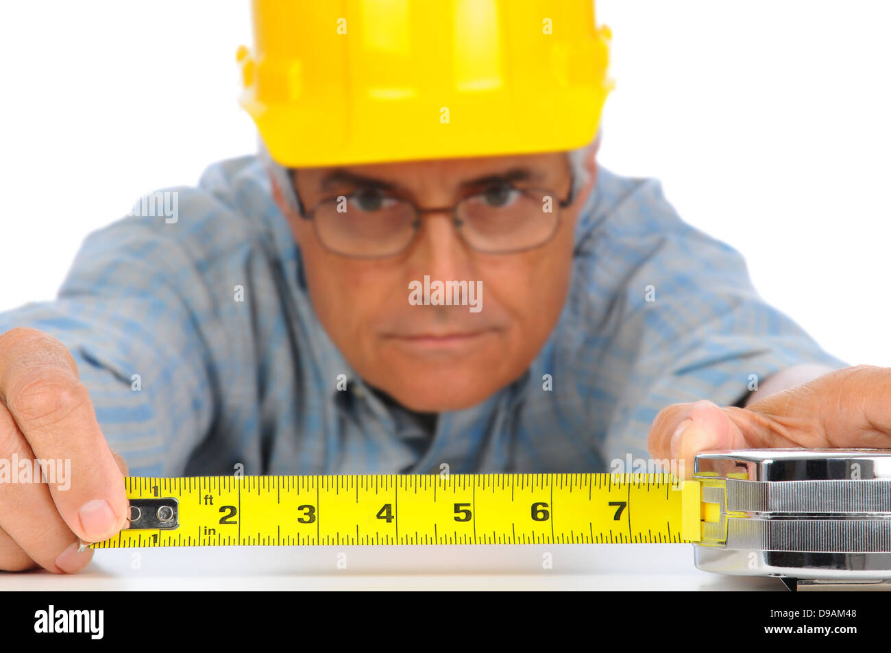 Closeup of a construction worker in hard hat using a measuring tape with the numbers facing forward. Stock Photo