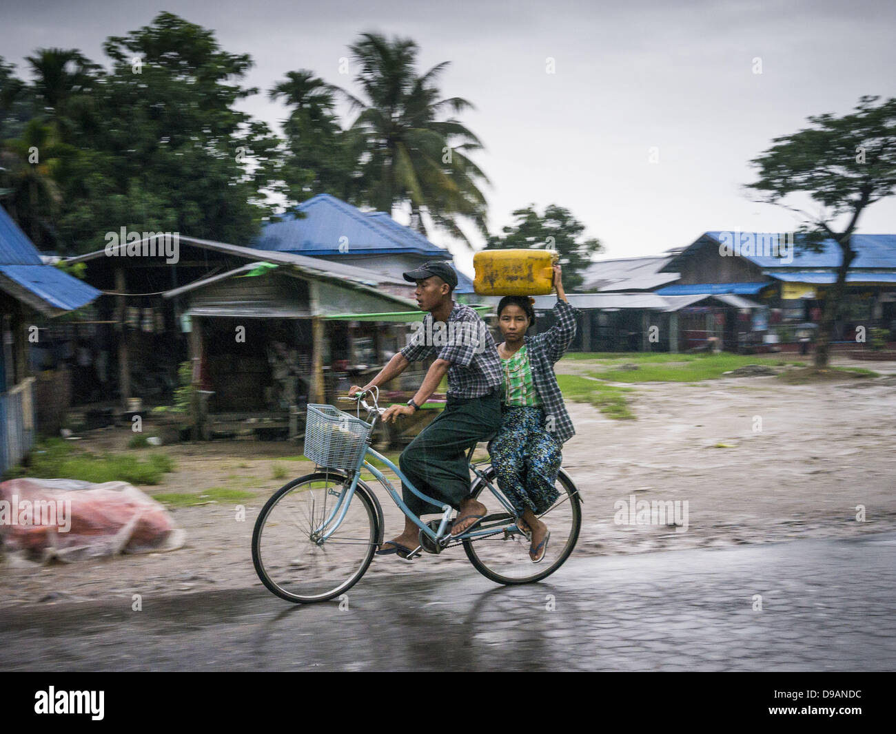 June 14, 2013 - Samalauk, Ayeyarwady, Union of Myanmar - A couple rides a bicycle through the rain along Highway 5 in Samalauk, Ayeyarwady, in the Irrawaddy delta region of Myanmar. This region of Myanmar was devastated by cyclone Nargis in 2008 but daily life has resumed and it is now a leading rice producing region. (Credit Image: © Jack Kurtz/ZUMAPRESS.com) Stock Photo