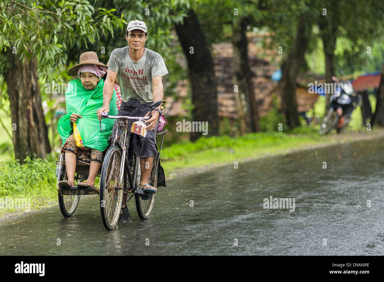 June 14, 2013 - Pantanaw, Ayeyarwady, Union of Myanmar - A gets a ride in a pedicab in the rain along Highway 5 in Pantanaw, Ayeyarwady, in the Irrawaddy delta region of Myanmar. This region of Myanmar was devastated by cyclone Nargis in 2008 but daily life has resumed and it is now a leading rice producing region. (Credit Image: © Jack Kurtz/ZUMAPRESS.com) Stock Photo