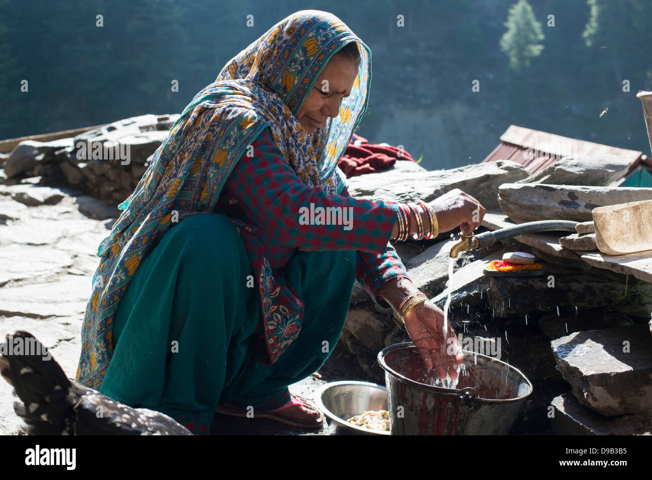 A Gaddi tribal matriarch washes the family's dishes at the Himalayan village of Kugti in Himachal Pradesh, India Stock Photo
