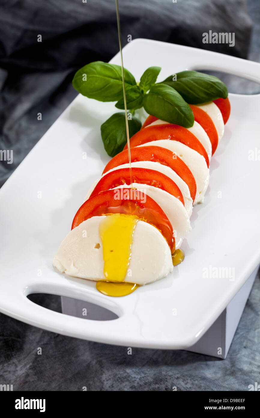 Slices of mozzarella cheese, tomatoes and basil herb on chopping board