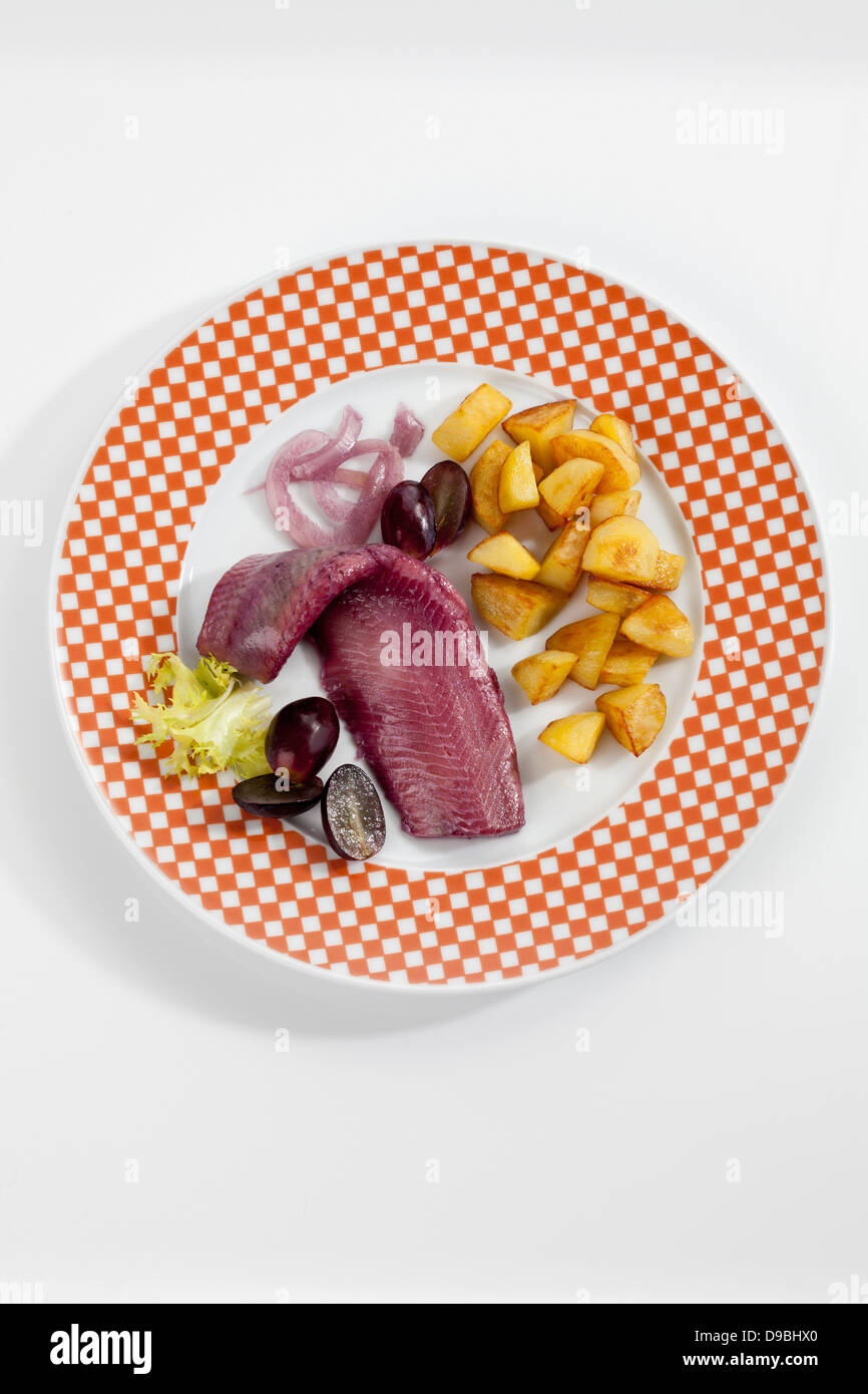 Sherry herring with roasted potatoes, onion and grapes on plate Stock Photo