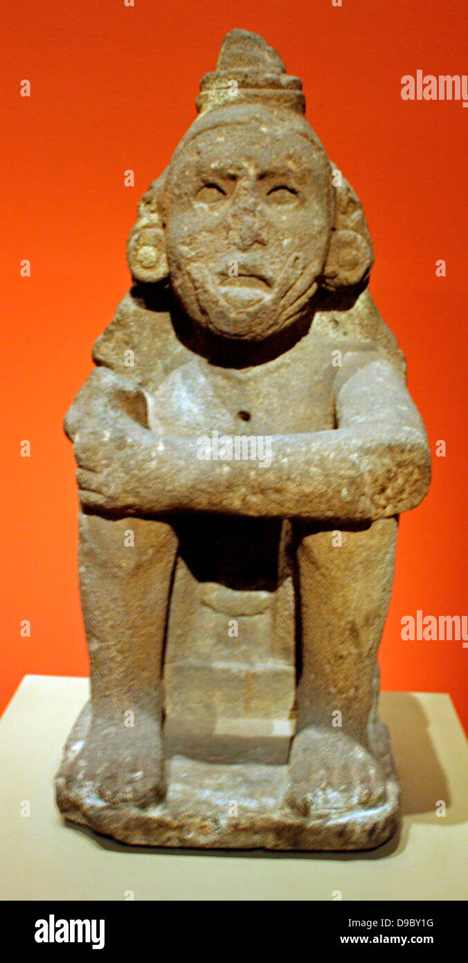 Aztec Standard Bearer. Seated on a small plinth with arms on knees and legs drawn up towards the body, this male figure wears an important headdress that was once topped with five tall tufts.  The tufts, related to the crest of a great curassow, are now missing, but in the back, the head covering still hangs onto the shoulders, where the figure's name, 5 Serpent, is carved. Stock Photo