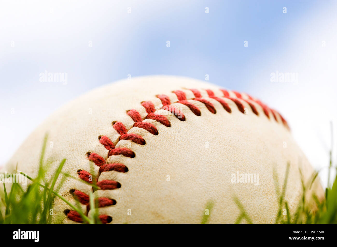 Close-up of a baseball lying in the grass against a partly cloudy sky Stock Photo