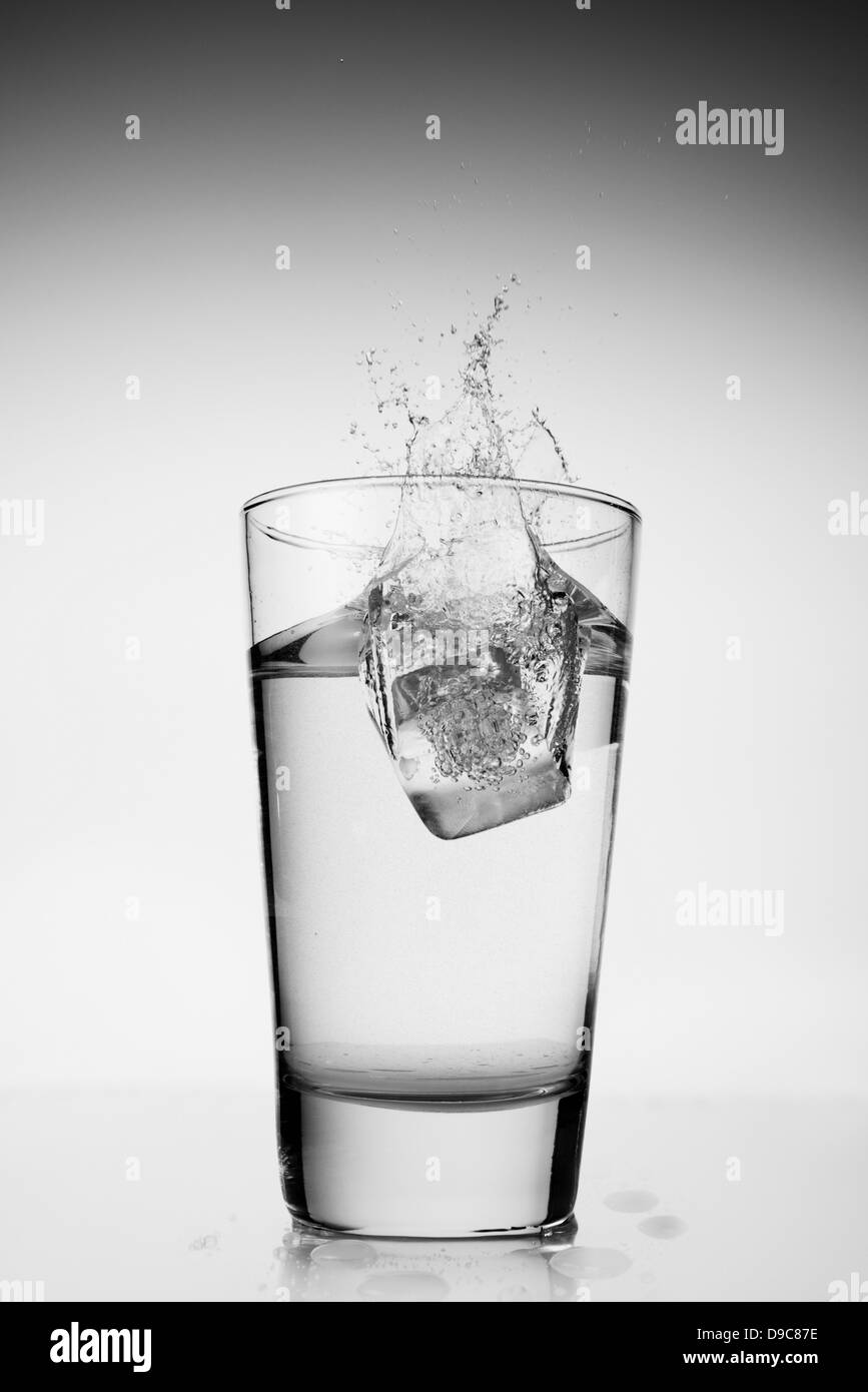 Ice cube falling into glass of water Stock Photo - Alamy