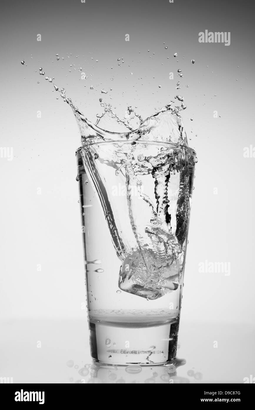 Ice cube falling into glass of water Stock Photo - Alamy