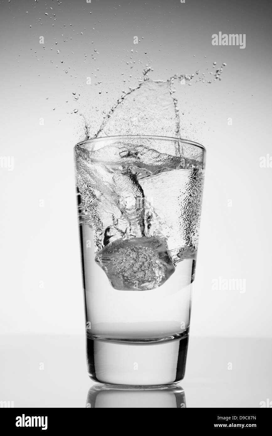 Ice cube falling into glass of water Stock Photo - Alamy