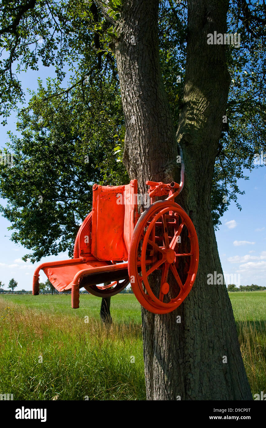 Wheel chair in a tree as a warning for too quickly moving motorcyclists, Wheelchair to a tree ace a warning for travelling too a Stock Photo