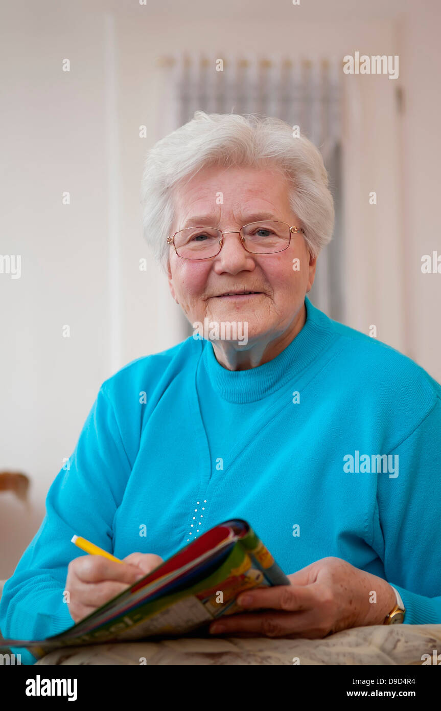 Germany, Berlin, Portrait of senior woman doing crossword, smiling Stock Photo