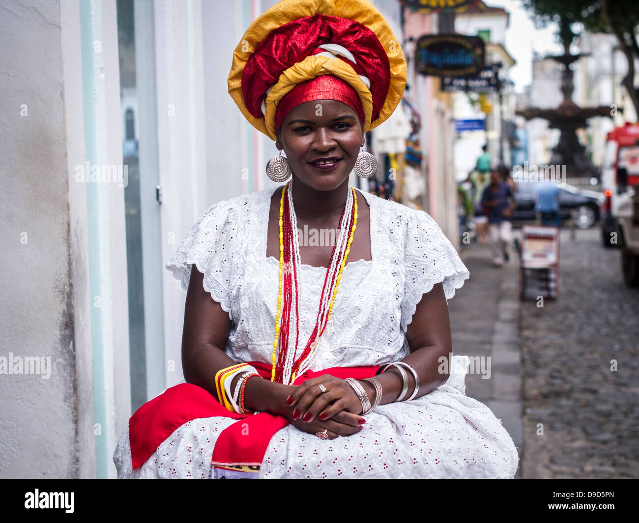 Woman wearing traditional clothes from the Bahia region of Brazil encourages tourists o buy souvenirs in Salvador. Stock Photo