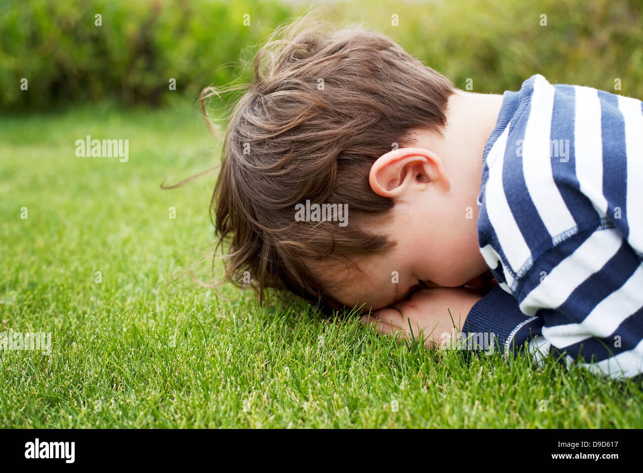 Male toddler hiding face down on grass Stock Photo