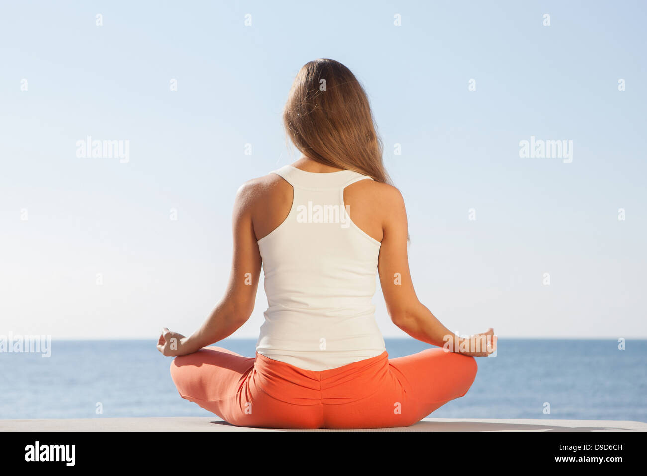 Young woman meditating by sea rear view Stock Photo - Alamy