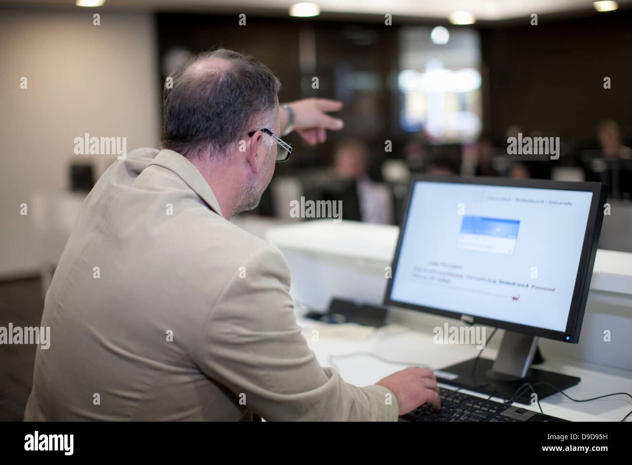 Lecturer using computer pointing to back of room Stock Photo - Alamy