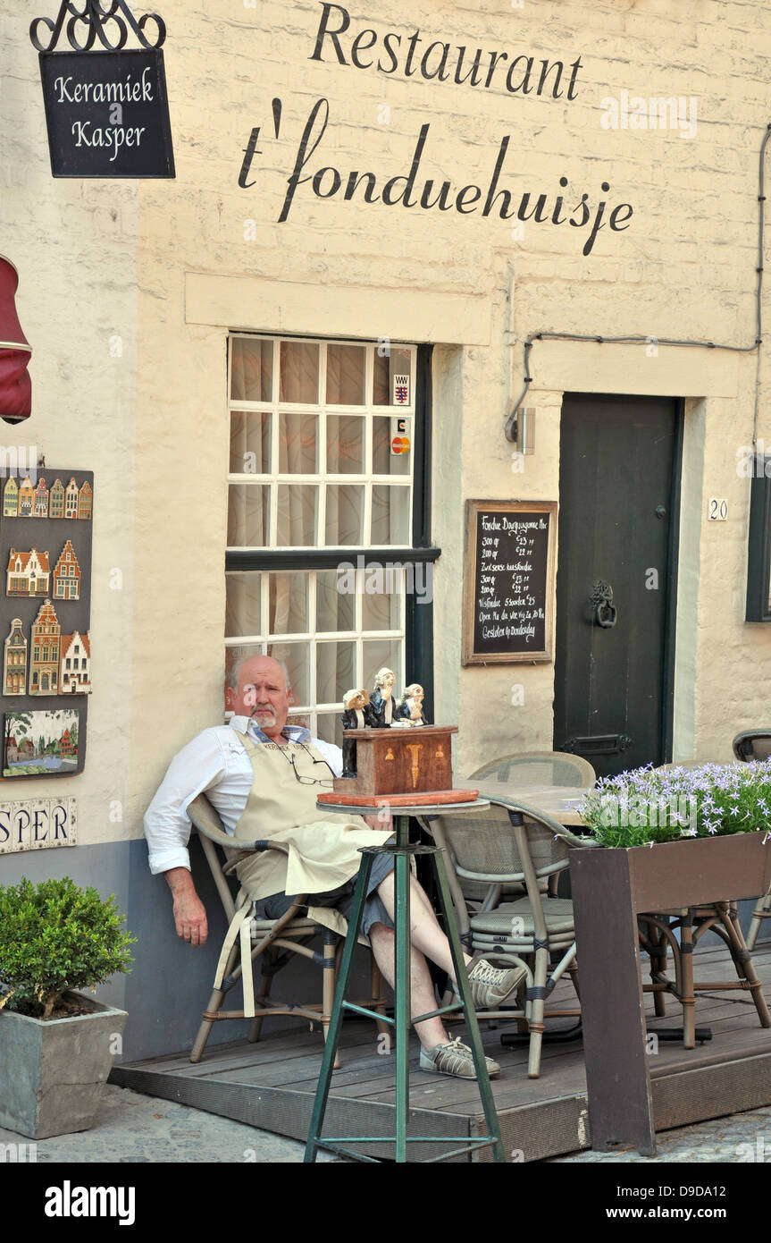 A man (probably the cook/chef) relaxing outside his restaurant in Bruges, Belgium, Europe. Stock Photo