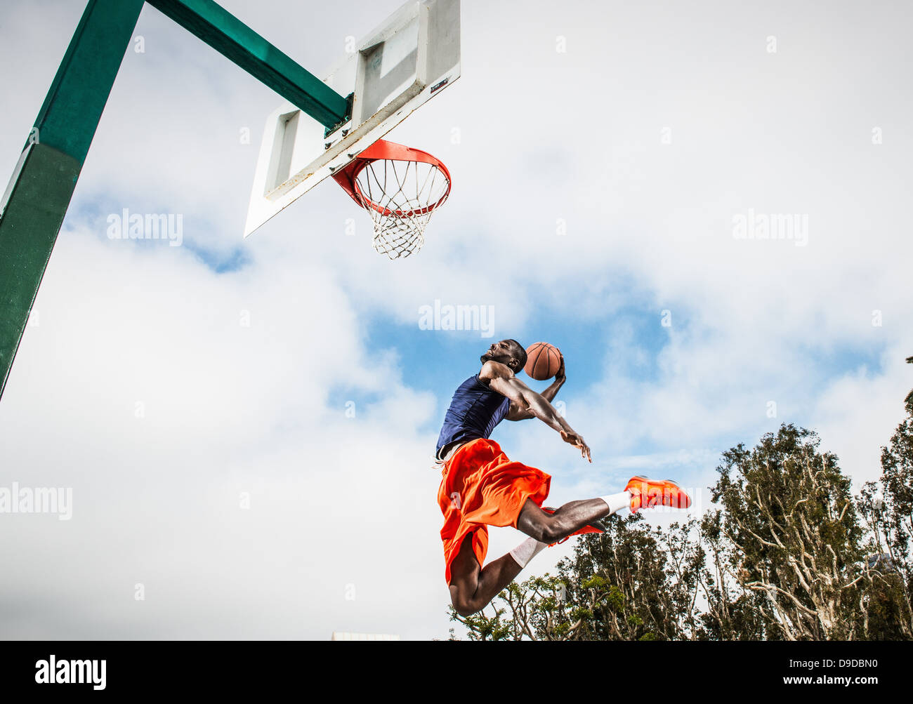Young man jumping to score hoop in basketball Stock Photo