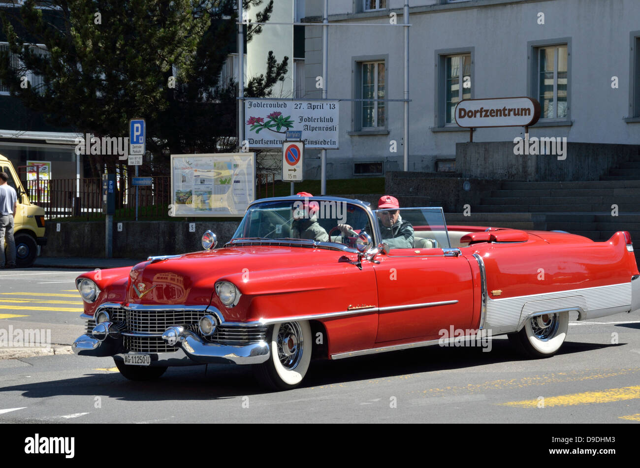 Elderly couple in vintage red Cadillac driving through the Swiss town of Einsiedeln. Stock Photo