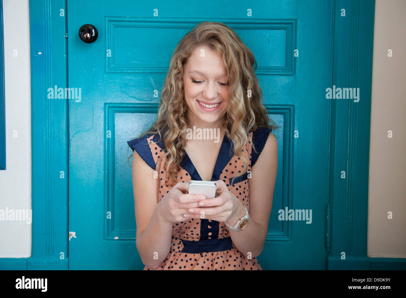 Teenager sitting in front of blue door, using mobile telephone Stock Photo