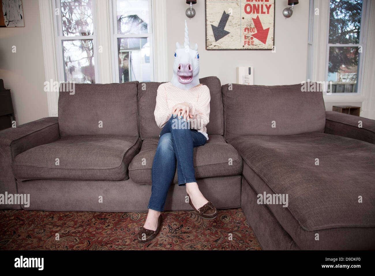 Girl sitting on sofa wearing unicorn head mask Stock Photo