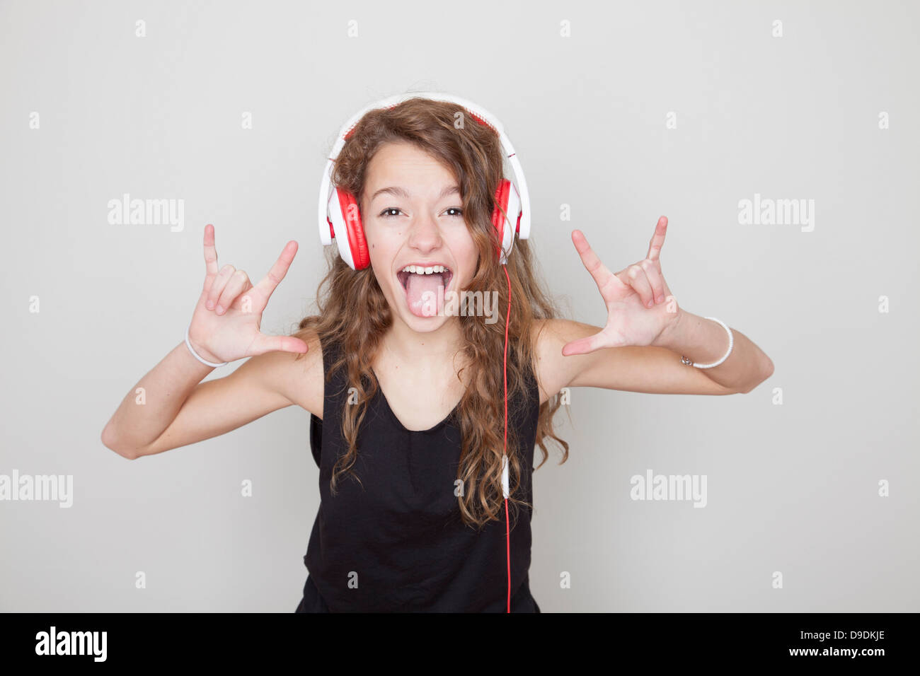 Girl wearing headphones making devil signs and sticking tongue out Stock Photo