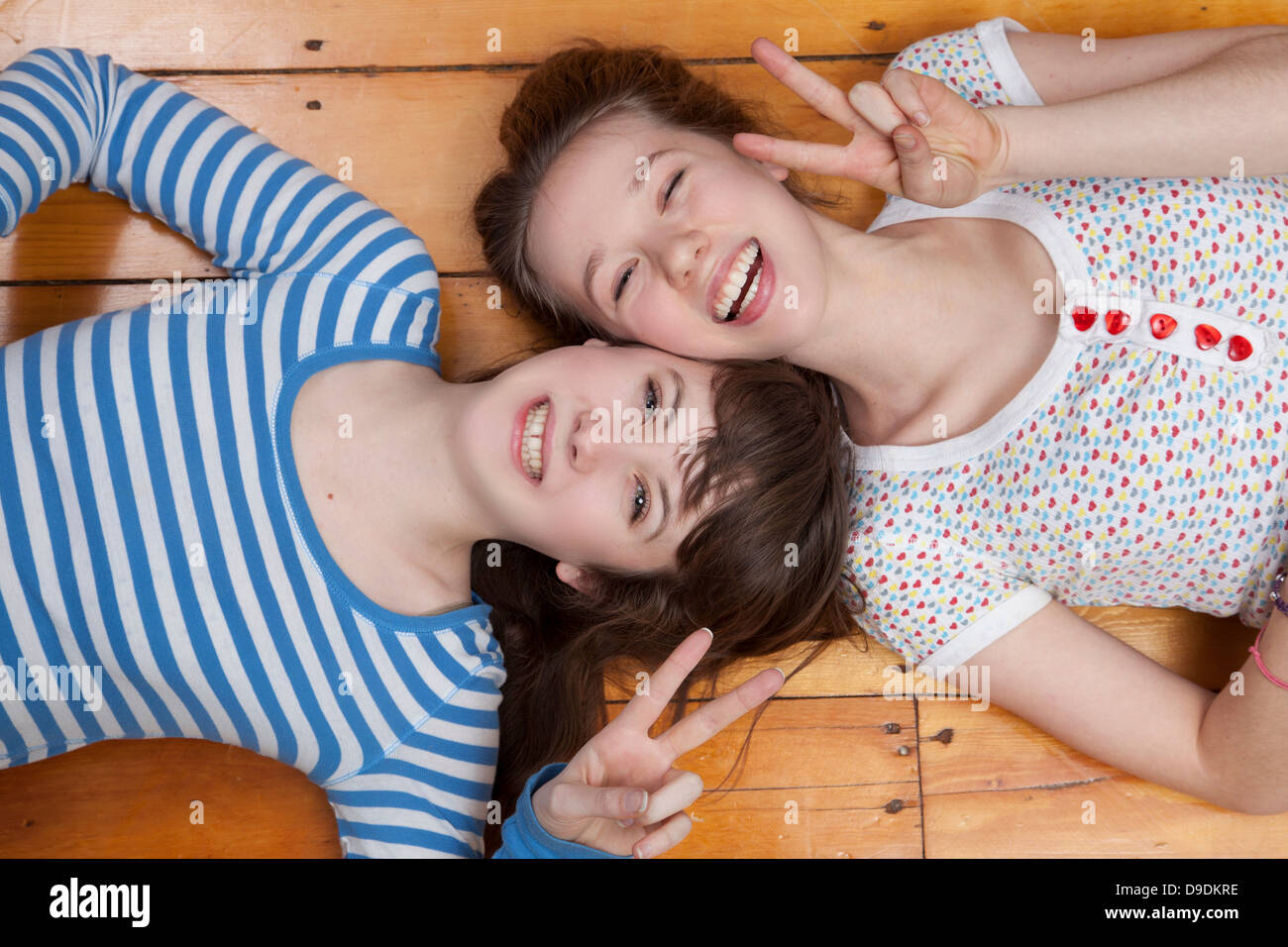 Girls lying on wooden floor doing peace signs Stock Photo