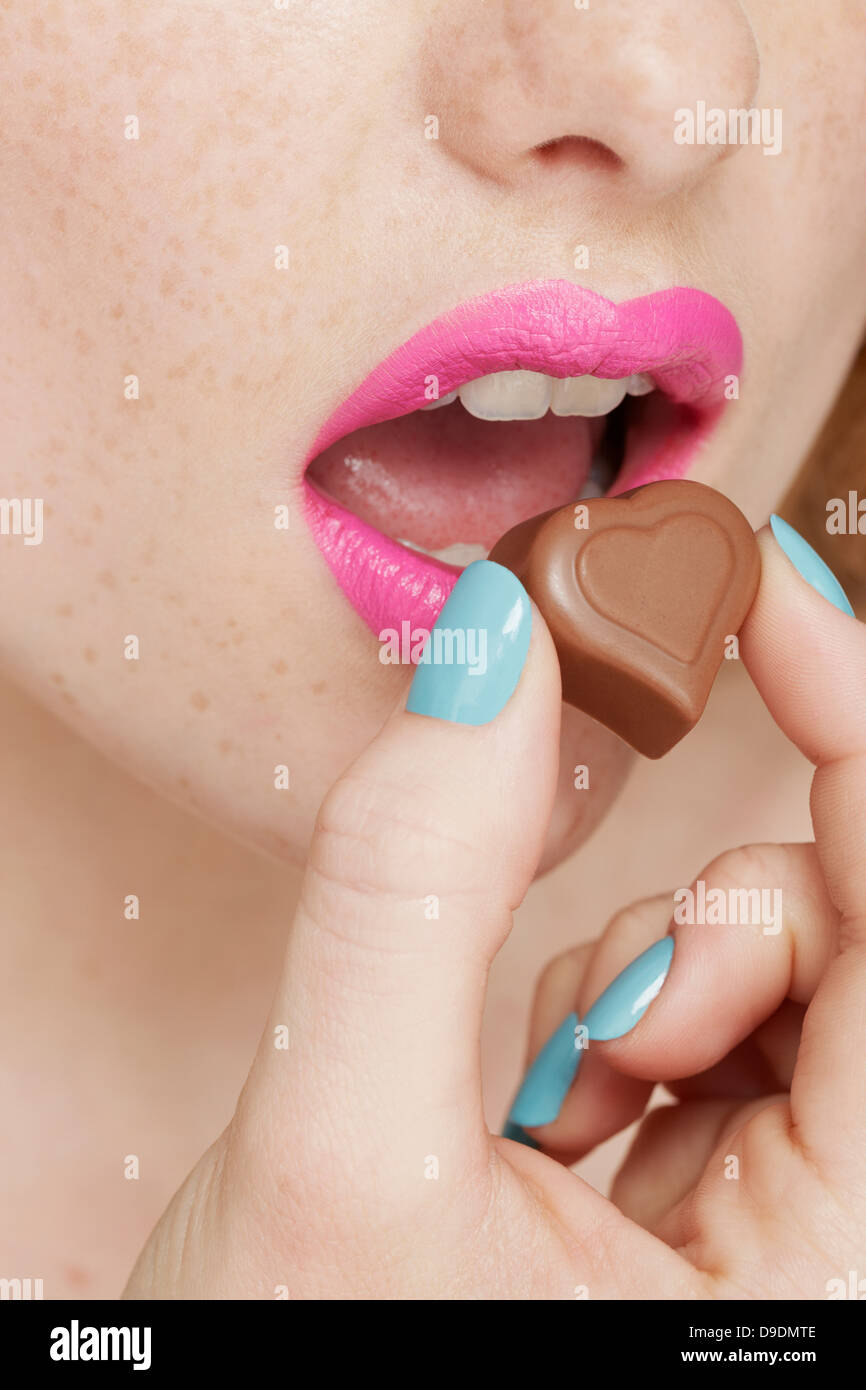 Woman wearing pink lipstick eating heart shaped chocolate Stock Photo