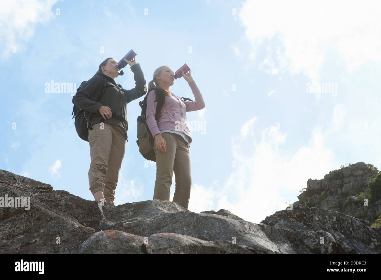 Two girl hikers drinking from flasks on top of rock formation Stock Photo