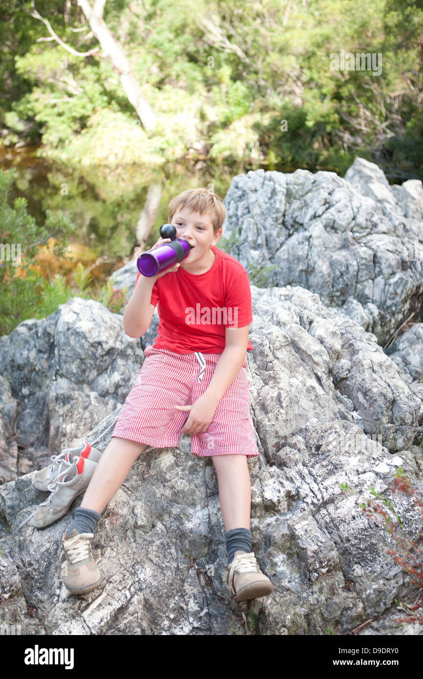 Portrait of young boy drinking from flask on rock Stock Photo - Alamy