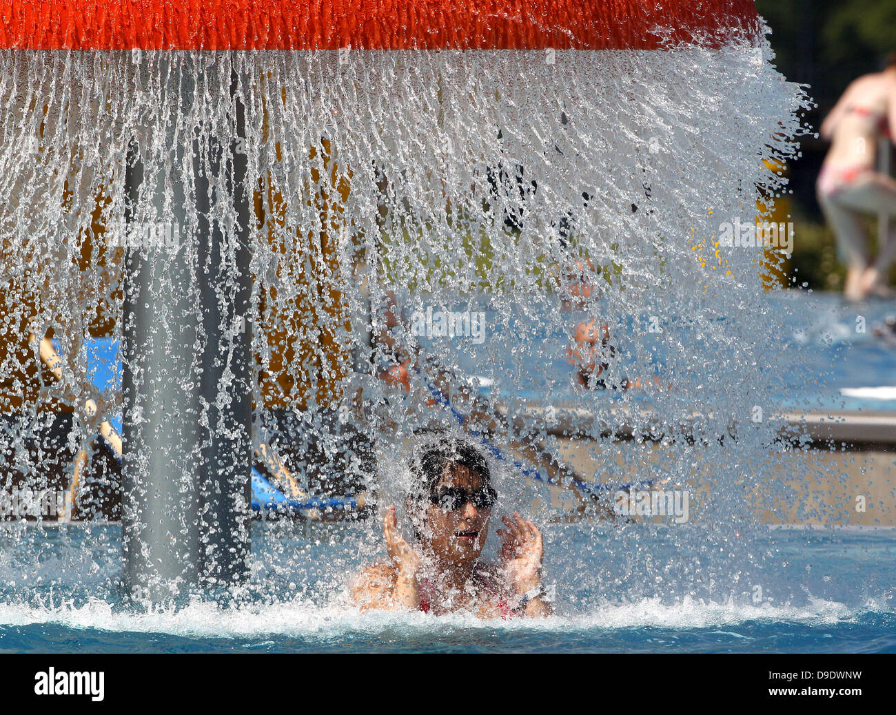 A bather refreshes hrself under a water fountain at openair swimming